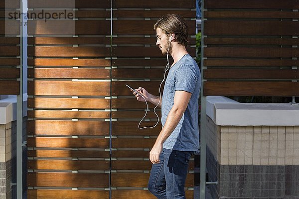 Junger Mann hört Musik auf dem Smartphone während des Spaziergangs