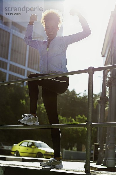 Fröhliche junge Sportlerin beim Stretching am Geländer auf der Straße