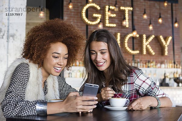 Freundinnen nutzen ein Smartphone mit Kaffee im Cafe