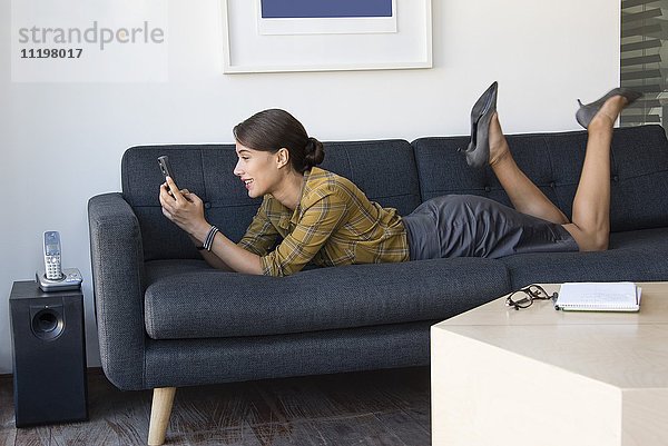 Glückliche Geschäftsfrau mit dem Handy auf der Couch