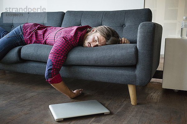 Junger Mann schläft auf Sofa mit Laptop