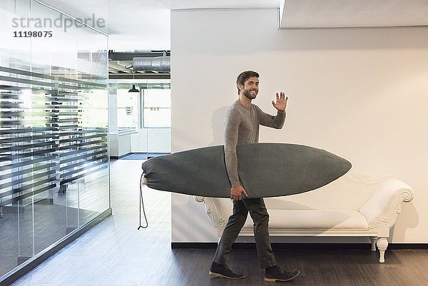Glücklicher junger Mann mit Surfbrett zu Hause