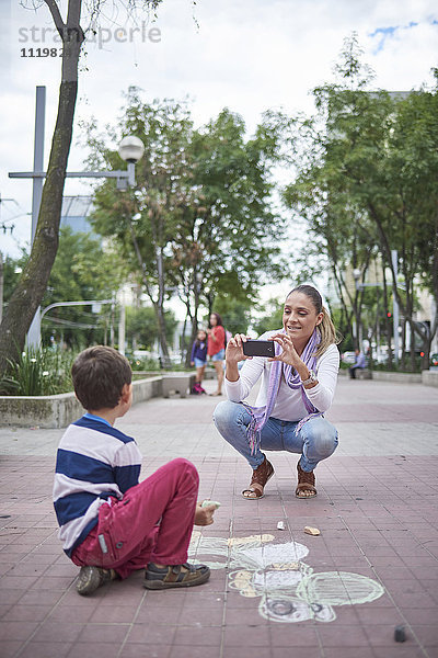 Hispanische Mutter fotografiert ihren Sohn auf dem Gehweg