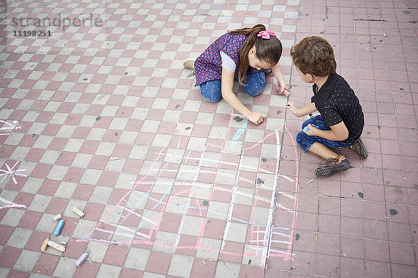 Hispanischer Junge und Mädchen zeichnen mit Kreide auf dem Bürgersteig