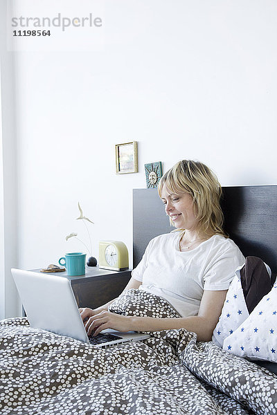 Kaukasische Frau mit Laptop im Bett