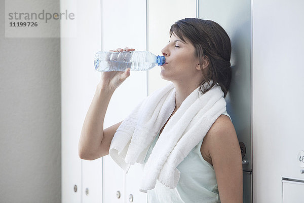 Frau trinkt Flaschenwasser in der Umkleidekabine