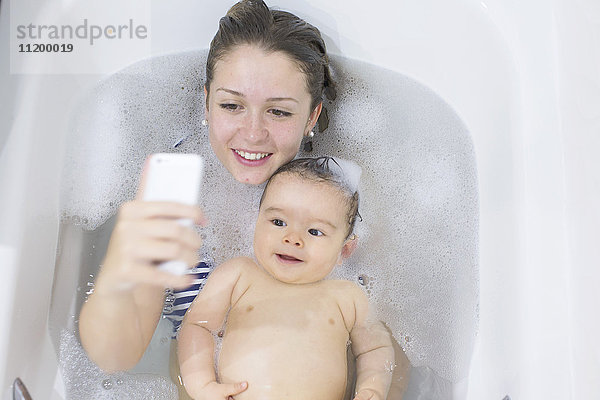 Mutter fotografiert sich und ihr Baby beim Baden mit dem Smartphone.