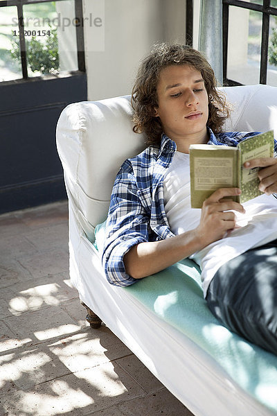 Junger Mann liest Buch auf der Couch
