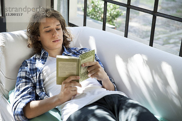 Junger Mann liest Buch auf der Couch
