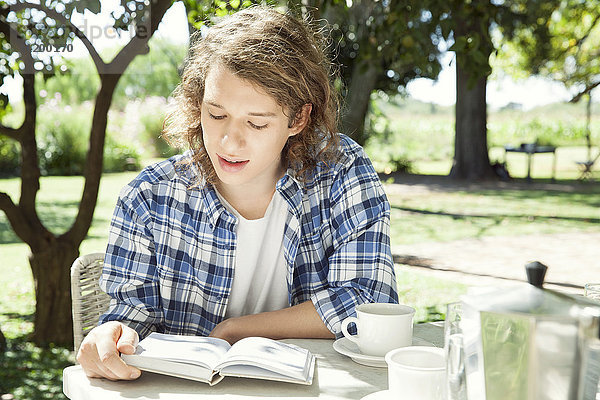 Junger Mann beim Lesen eines Buches bei einer Tasse Kaffee