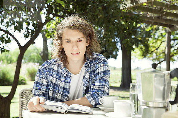 Junger Mann am Frühstückstisch im Freien mit Buch