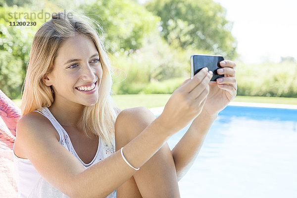 Frau  die einen Selfie am Pool mit dem Smartphone nimmt