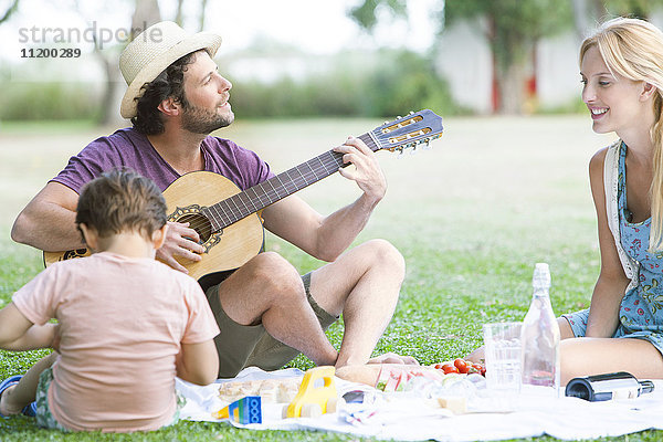 Mann spielt Akustikgitarre neben Frau und Sohn