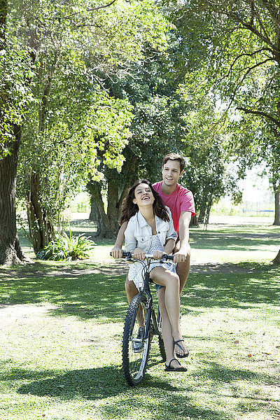 Junges Paar beim Radfahren zusammen mit der Freundin sitzend im Damensattel auf der Querlatte