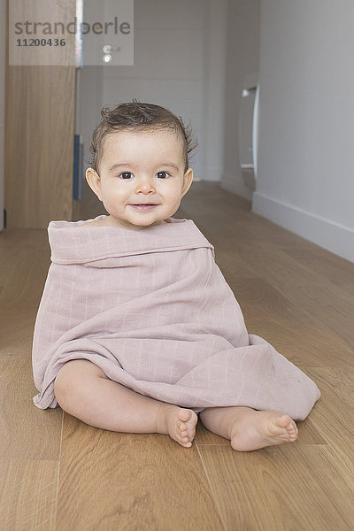 Baby auf dem Boden sitzend  in eine Decke gehüllt  Portrait