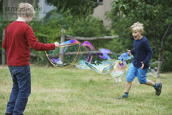 Glückliche Brüder spielen mit Seifenblase im Hinterhof