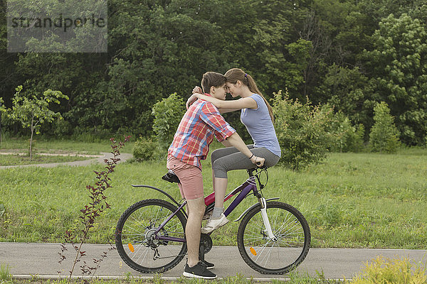 Romantisches Paar auf dem Fahrrad gegen Bäume im Park sitzend