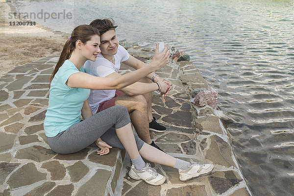 Liebende Paare  die am See in der Stadt sitzen und Selfie nehmen.