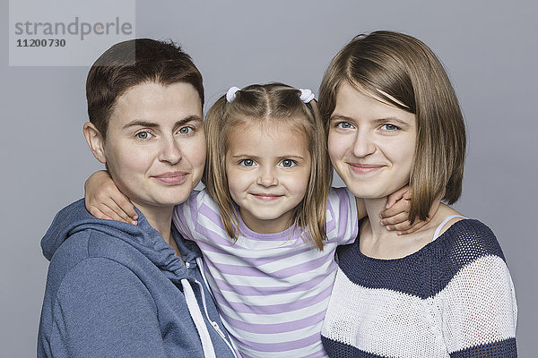 Porträt eines lächelnden Mädchens mit Mutter und Schwester vor grauem Hintergrund
