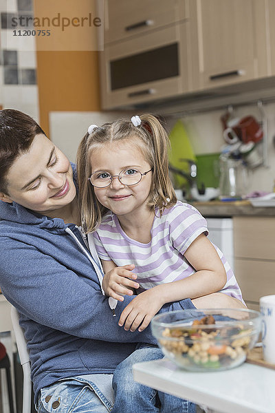 Mutter sieht lächelndes Mädchen beim Frühstück zu Hause an.