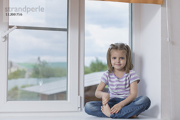 Porträt eines süßen Mädchens  das auf dem Fensterbrett sitzt.