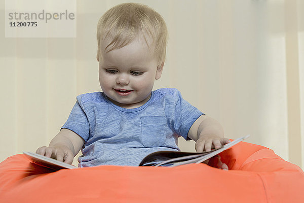 Nahaufnahme des süßen  lächelnden Mädchens beim Lesen eines Buches  während es zu Hause auf einem Bohnensack sitzt.