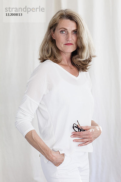 Porträt einer selbstbewussten reifen Frau am weißen Vorhang