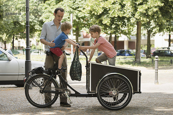 Jungen spielen auf dem Fahrrad von Vater  der auf der Straße steht.