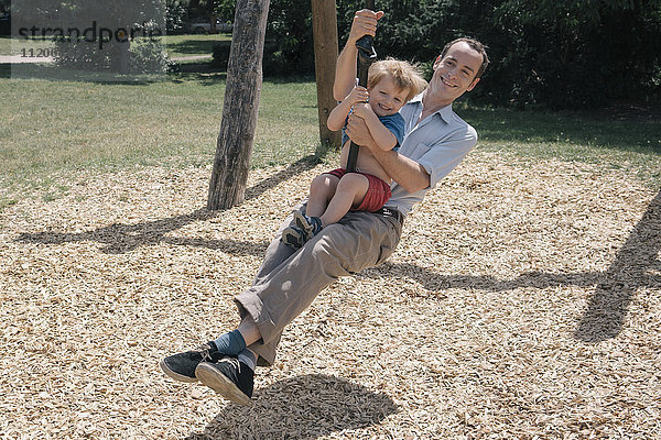 Fröhlicher Vater schwingt mit Sohn auf dem Spielplatz