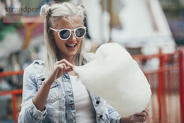 Modische junge Frau mit Sonnenbrille  die im Freien Zuckerwatte isst.