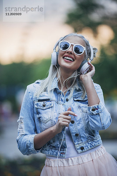 Fröhliche modische Frau mit Sonnenbrille beim Musikhören über Kopfhörer