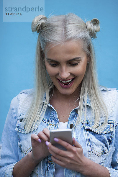 Fröhliche modische junge Frau mit Handy gegen die blaue Wand