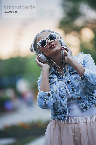 Modische junge Frau mit Sonnenbrille beim Musikhören über Kopfhörer