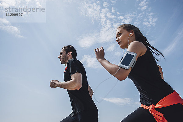 Niederwinkelansicht eines jungen Mannes und einer jungen Frau beim Joggen gegen den Himmel