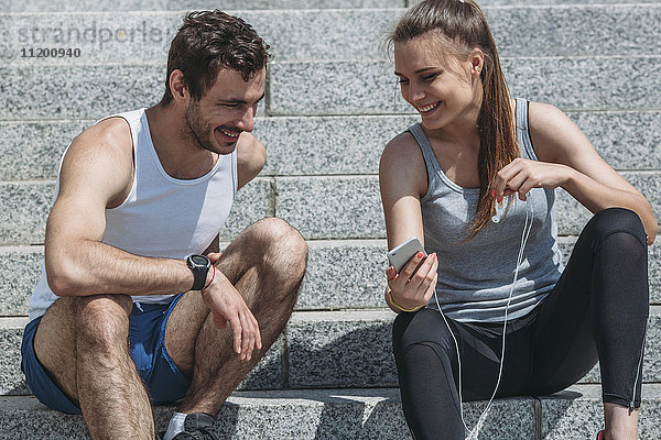 Fröhliche Frau zeigt Smartphone dem männlichen Freund beim Sitzen auf der Treppe