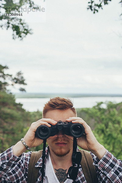 Nahaufnahme eines jungen Mannes mit Fernglas beim Wandern im Wald gegen den Himmel