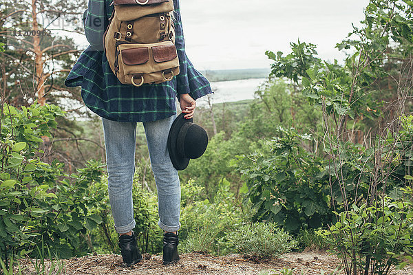 Niedriger Teil der Backpackerin  die den Hut hält  während sie im Wald steht.