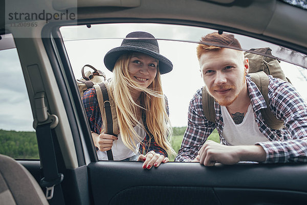Lächelnde männliche und weibliche Rucksacktouristen schauen in die Autoscheibe