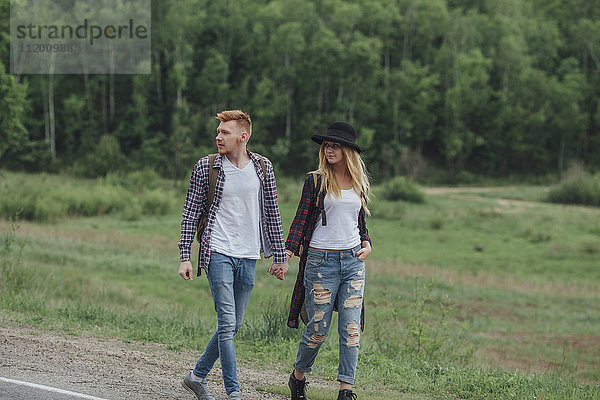 Paar  das sich an den Händen hält  während es am Straßenrand durch den Wald geht.
