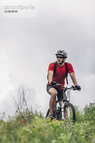 Selbstbewusster Mann auf dem Mountainbike gegen bewölkten Himmel