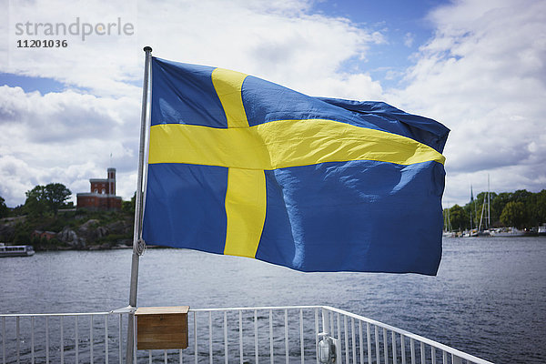 Schwedische Flagge am Geländer mit Wasser gegen bewölkten Himmel