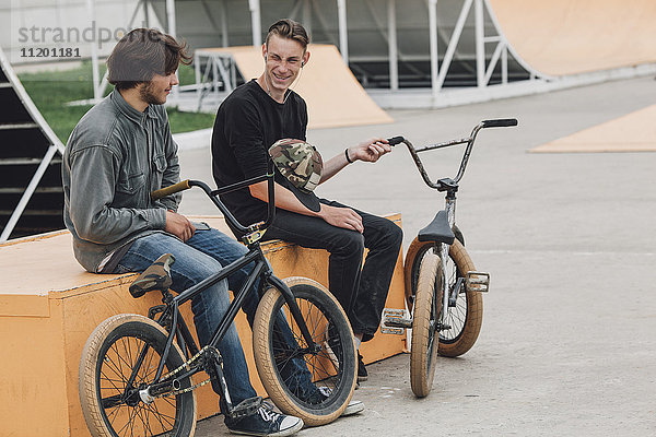 Fröhliche Freunde auf dem Sitz mit Fahrrädern im Skateboard-Park