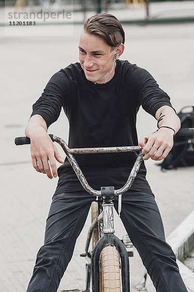 Lächelnder Teenager sitzend auf dem Fahrrad im Skateboard-Park