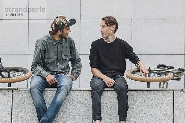 Freunde beim Sitzen mit Fahrrädern an der Wand im Skateboardpark