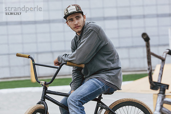 Nachdenklicher Teenager sitzt auf dem Fahrrad im Skateboard-Park.