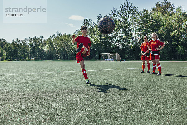 Fußballspieler tritt Ball  während Freunde in der Nähe auf dem Spielfeld stehen