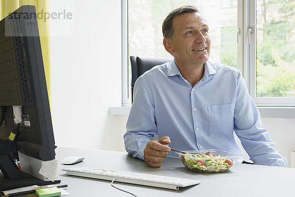 Lächelnder Geschäftsmann beim Salat am Schreibtisch im Kreativbüro