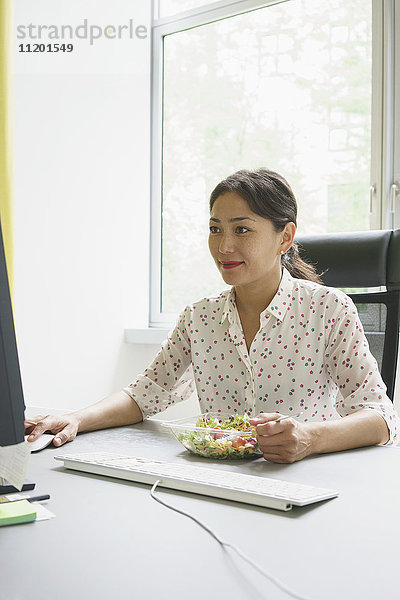 Geschäftsfrau mit Computer und Salat am Schreibtisch