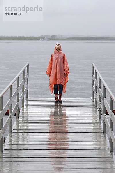 Frau im Regenmantel am Steg während der Regenzeit