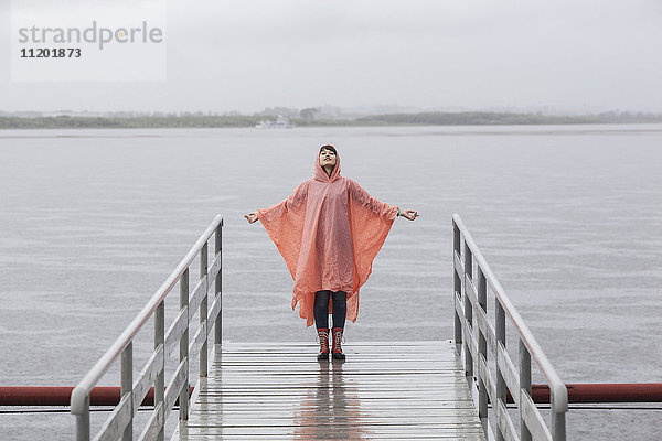 Frau im Regenmantel genießt Regenzeit am Steg